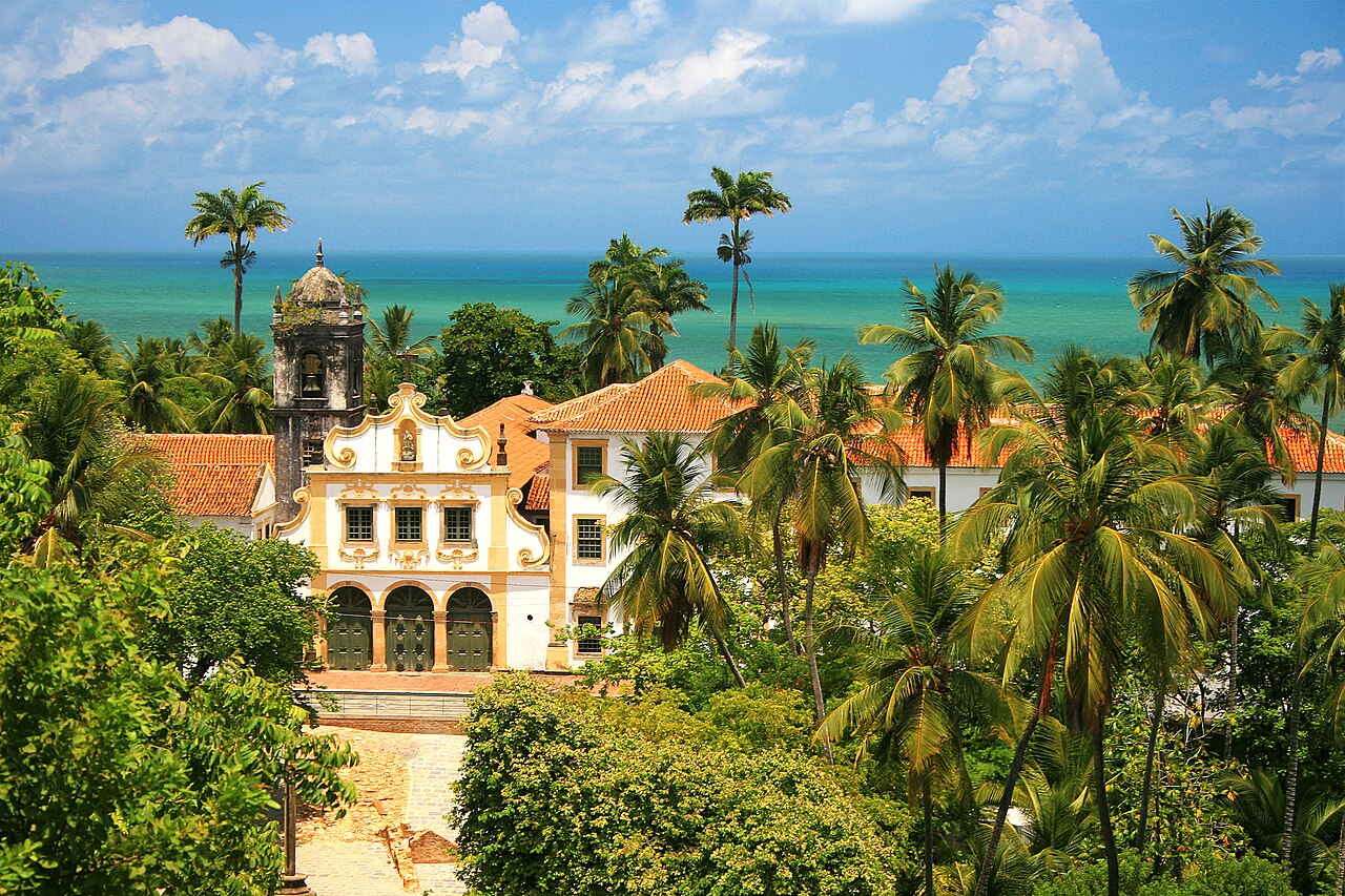 Convento de São Francisco em Olinda, fachada branca e amarela, palmeiras e o mar ao fundo.